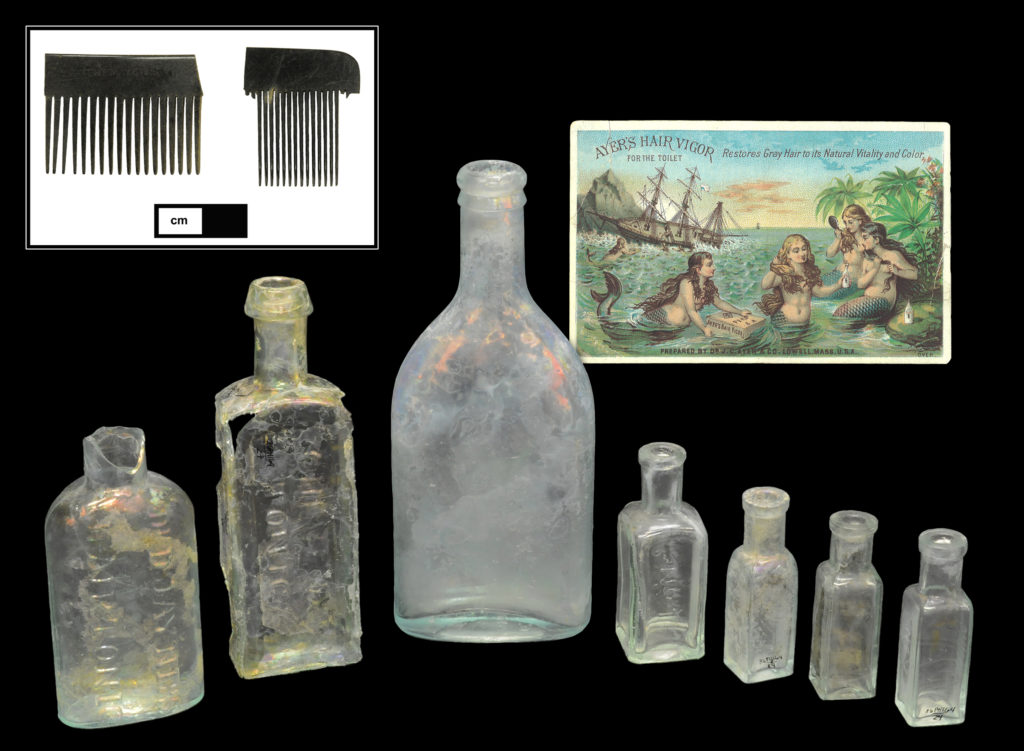Hair products and accessories: (Top, left) Fragments of two small hard rubber combs (Cat # 4.29.60, 4.31.108). (Bottom, left to right) Dr. D. Jayne’s Hair Tonic bottle (4A-G-0052); G. Cane’s Cheveux Tonic bottle; Ayer’s Hair Vigor bottle (4A-G-0298) and example of a trade card for Ayer’s Hair Vigor depicting similar bottle form, dating between 1875 and 1890; J. Hambleton & Son “No. 1” hair dye bottle; and three J. Hambleton & Son “No. 2” hair dye bottles (4A-G-0017, 4A-G-0006, 4A-G-0007, 4A-G-0037). 