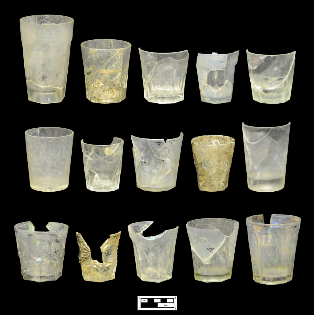 Assortment of colorless glass tumblers: (Top row, left to right) Six flutes (4A-G-0292); eight flutes, one of a set of four (4A-G-0270); nine flutes, one of three (4A-G-0252); six square top flutes, one of two (4A-G-0266); nine cut flutes, one of five (4A-G-0247). (Middle row, left to right) Plain pressed starburst base (4A-G-0134); band of 12 small flutes around base, one of two (4A-G-0242); faintly pressed pattern, two rows fluting (4A-G-0262); unidentified early pressed pattern (4A-G-0128); plain with concave base (4A-G-0244). (Bottom row, left to right) Ashburton pattern, one of three (4A-G-0260); Chilson pattern (4A-G-0256); six flutes (4A-G-0254); eight flutes (4A-G-0257); Pillar pattern (4A-G-0267).
